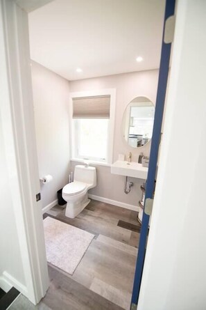 A bathroom with a toilet, sink, and mirror. - Stylish Treetop Loft with Balcony and Ocean Views (Harpswell)