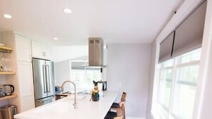 A modern kitchen with a central island, stainless steel appliances, and wooden flooring. - Modern Cottage with Ocean Access & Wildlife (Harpswell)