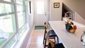 A modern kitchen with a long countertop, wooden chairs, and a view of the outdoors through large windows. - Modern Cottage with Ocean Access & Wildlife (Harpswell)