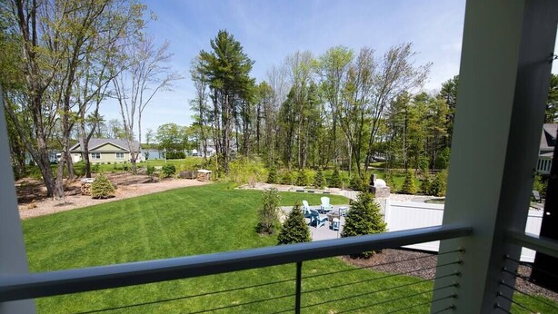 A balcony with a view of a well-maintained lawn, trees, and a distant house. - Modern Cottage with Ocean Access & Wildlife (Harpswell)