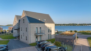 Um edifício moderno de dois andares com telhado inclinado, janelas amplas e vista para um lago.