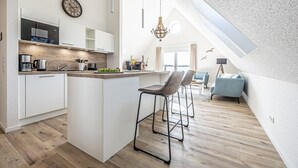Uma cozinha moderna com armários brancos, uma ilha central e um espaço de refeições com sofá e cadeiras azuis.