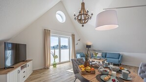 Uma sala de estar moderna com televisão, mesa de jantar com frutas e um sofá azul.