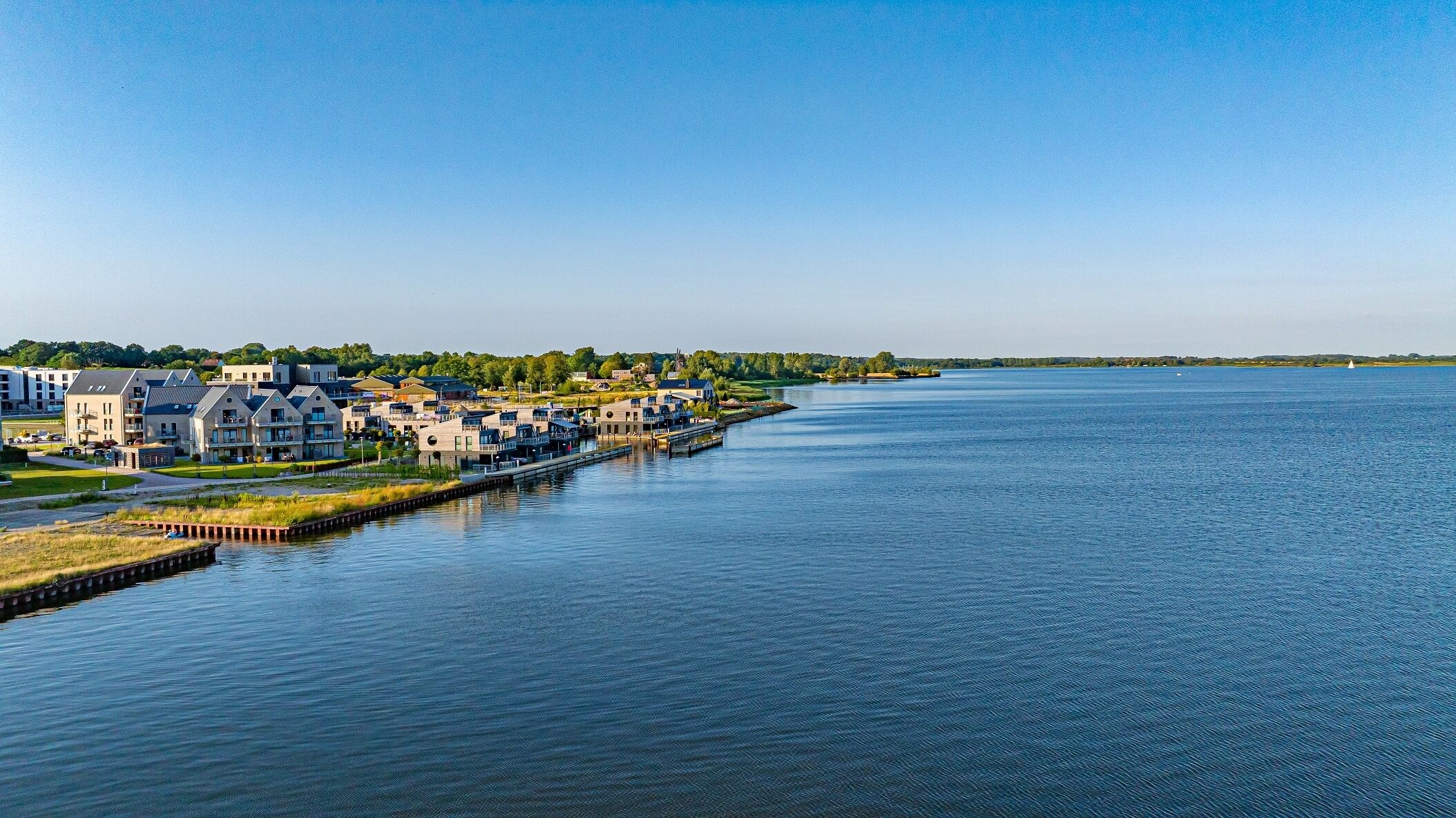 Zona residencial frente al río con casas modernas, un muelle y un río tranquilo.