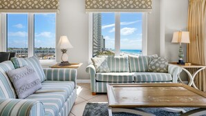 Una sala de estar moderna con sofás a rayas, una mesa de centro de madera y amplios ventanales con vistas a la playa y al paisaje urbano.