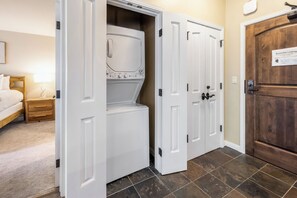 A room with a bed, a nightstand, a built-in washer-dryer unit, and a wooden door with a business license sign.