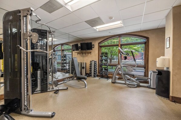 Une salle de sport équipée de matériel d’exercice, de miroirs et de fenêtres.