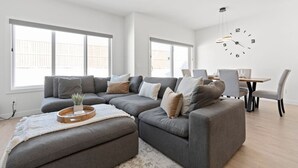 Una sala de estar moderna con un sofá seccional, una mesa de comedor con sillas y un reloj de pared grande.