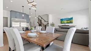 Una cocina moderna con armarios grises, una mesa de comedor de madera dispuesta para cuatro personas y un sofá gris en la sala de estar.