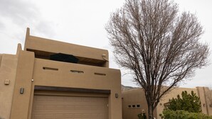 Un edificio moderno con una puerta de garaje grande, un árbol en primer plano y un paisaje desértico al fondo.