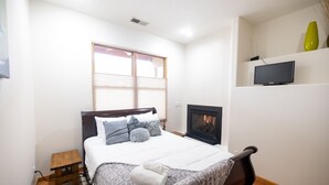 Un dormitorio con una cama, una mesita de noche pequeña, un televisor en un estante y una chimenea.