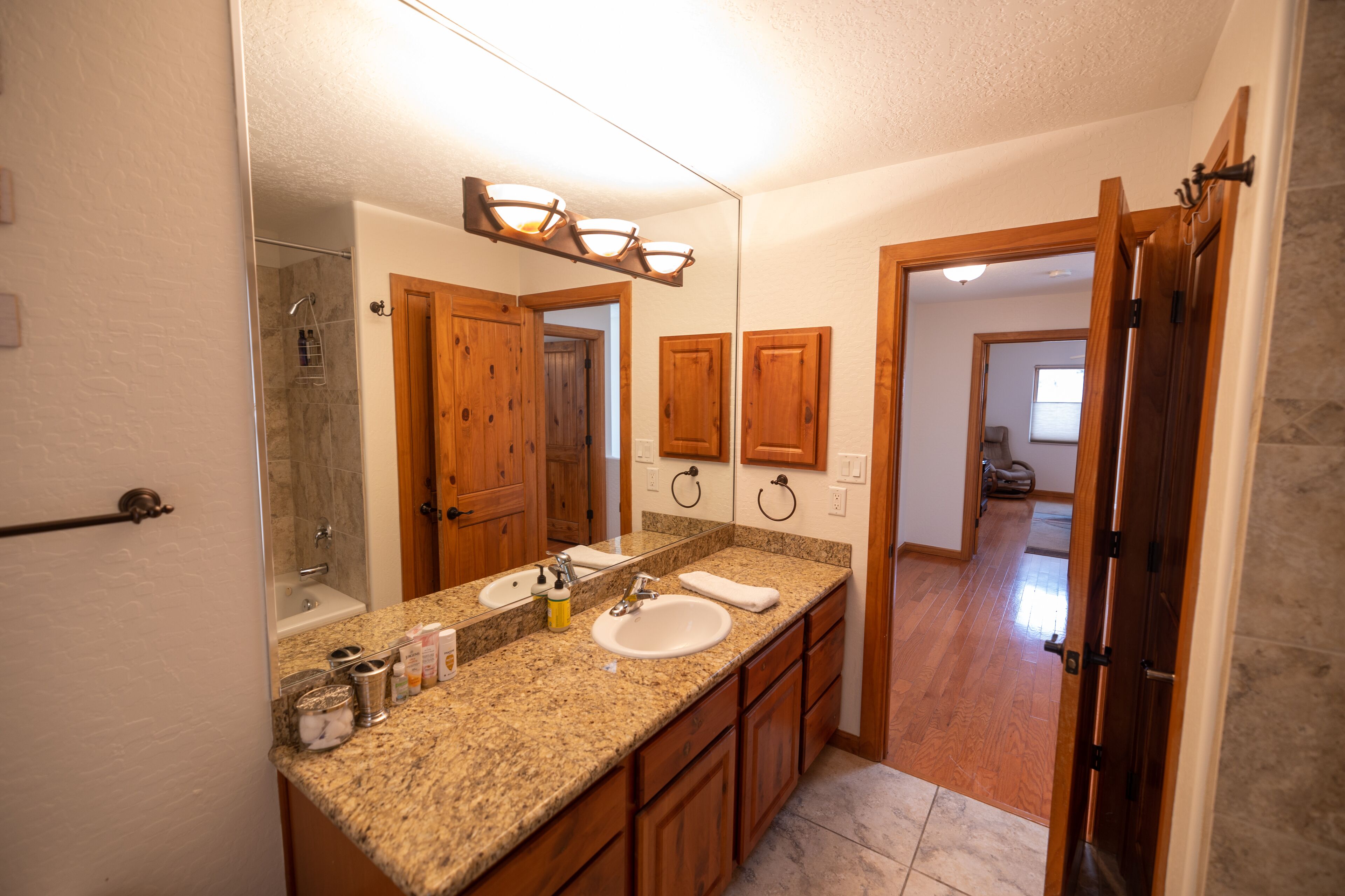 A bathroom with a granite countertop, double sink, wooden cabinets, and a large mirror.