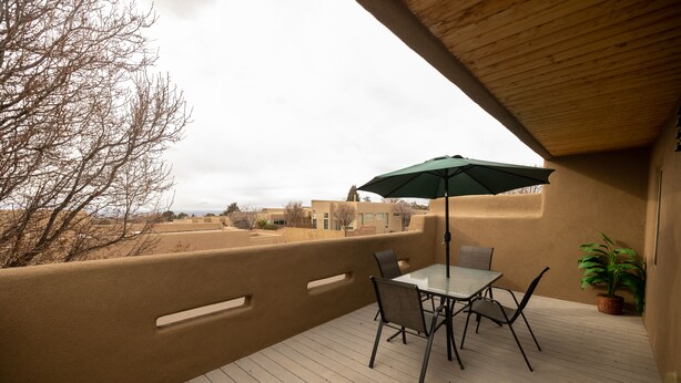 Una terraza de madera con una mesa, sillas, un paraguas verde y una planta en maceta.