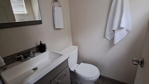 Ein kleines Badezimmer mit Waschbecken, Waschtisch und Toilette in Weiß. Ein Handtuch hängt an der Wand, und ein Spiegel spiegelt einen Teil des Raumes wider.