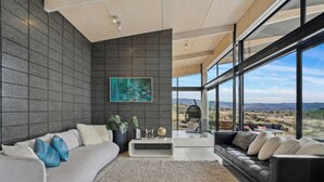Ett modernt vardagsrum med en grå soffa, en svart lädersoffa, ett soffbord och ett stort fönster med utsikt över landskapet.
