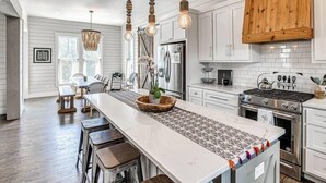 Une cuisine moderne avec des meubles blancs, un îlot central, des luminaires suspendus et une poutre en bois au plafond.