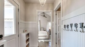 Un couloir avec un lustre, un lit en arrière-plan et un porte-manteau orné de lettres.