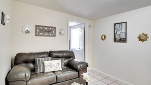 A living room with a brown leather sofa, a coffee table with a vase, and wall decorations including a framed picture and two wall sconces. - Lakeland Vacation Rental: 38 Mi to Disney! (Lakeland)
