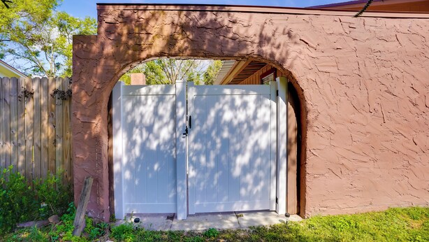 A white garage door with a brown textured wall and a wooden fence in the background. - Lakeland Vacation Rental: 38 Mi to Disney! (Lakeland)