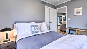 A bedroom with a bed, nightstand, lamp, and a door leading to another room. - Charming Rocky Point Home ~ 1 Mi to Beach! (Rocky Point)