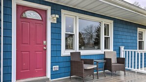 A blue house with a red door, white window frames, and a porch with wicker chairs and a table. - Charming Rocky Point Home ~ 1 Mi to Beach! (Rocky Point)