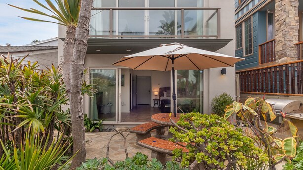 Ein zweistöckiges Haus mit einer Terrasse, ausgestattet mit einem Tisch und Sonnenschirm.