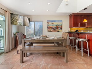 Una cocina moderna con una mesa de comedor para cuatro, una barra con taburetes y un ventanal con vistas al exterior.