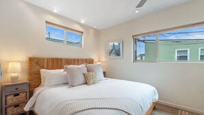 Ein Schlafzimmer mit einem großen Bett, einem Nachttisch mit Lampe, einem Deckenventilator und zwei Fenstern mit Blick ins Freie.