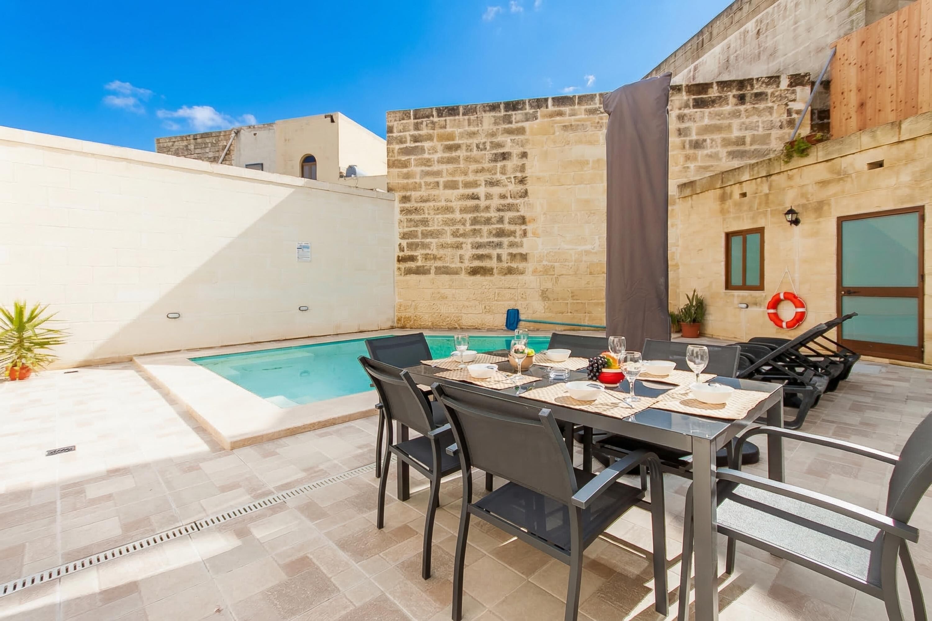 Un espace extérieur aménagé pour les repas, avec une piscine, des murs en pierre et un ciel dégagé.