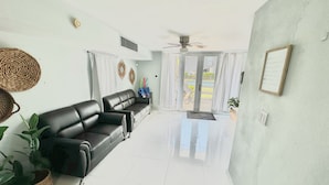 A spacious living room with a black leather sofa, a ceiling fan, and a view through large glass doors to an outdoor area. - Eco-Luxury Villa with Pool, Beach Access, and 24 hour I uninterrupted power (Dorado)