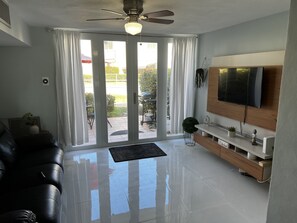 A modern living room with a black leather sofa, a TV mounted on the wall, and a sliding glass door leading to an outdoor area.