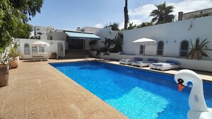 Ein Pool mit Liegestühlen und Sonnenschirmen, umgeben von weißen Wänden und Kübelpflanzen.