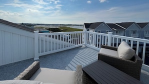 A balcony with a white railing, wicker furniture, and a view of houses and a body of water.