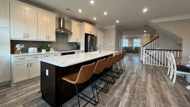 A modern kitchen with a central island, bar stools, and a dining area with a staircase.