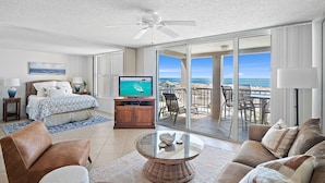 Habitación de hotel con cama, televisión, zona de estar y balcón con vista al océano.