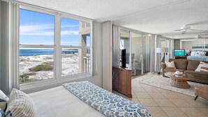 Amplia sala de estar con un ventanal con vista a la playa, un sofá, un televisor y un aparador de madera.