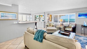 Un salon moderne avec un canapé beige, une table basse et une vue sur l’océan grâce à de grandes fenêtres.