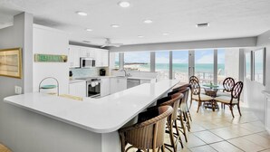 Une cuisine moderne dotée d’un grand îlot central, de meubles blancs et offrant une vue sur l’océan.