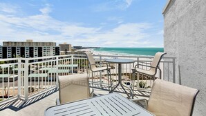 Un balcon avec vue sur une plage et l’océan, comprenant une table et des chaises.