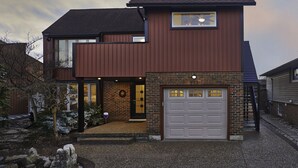 Une maison à deux étages avec un garage, une façade en briques et un petit jardin.