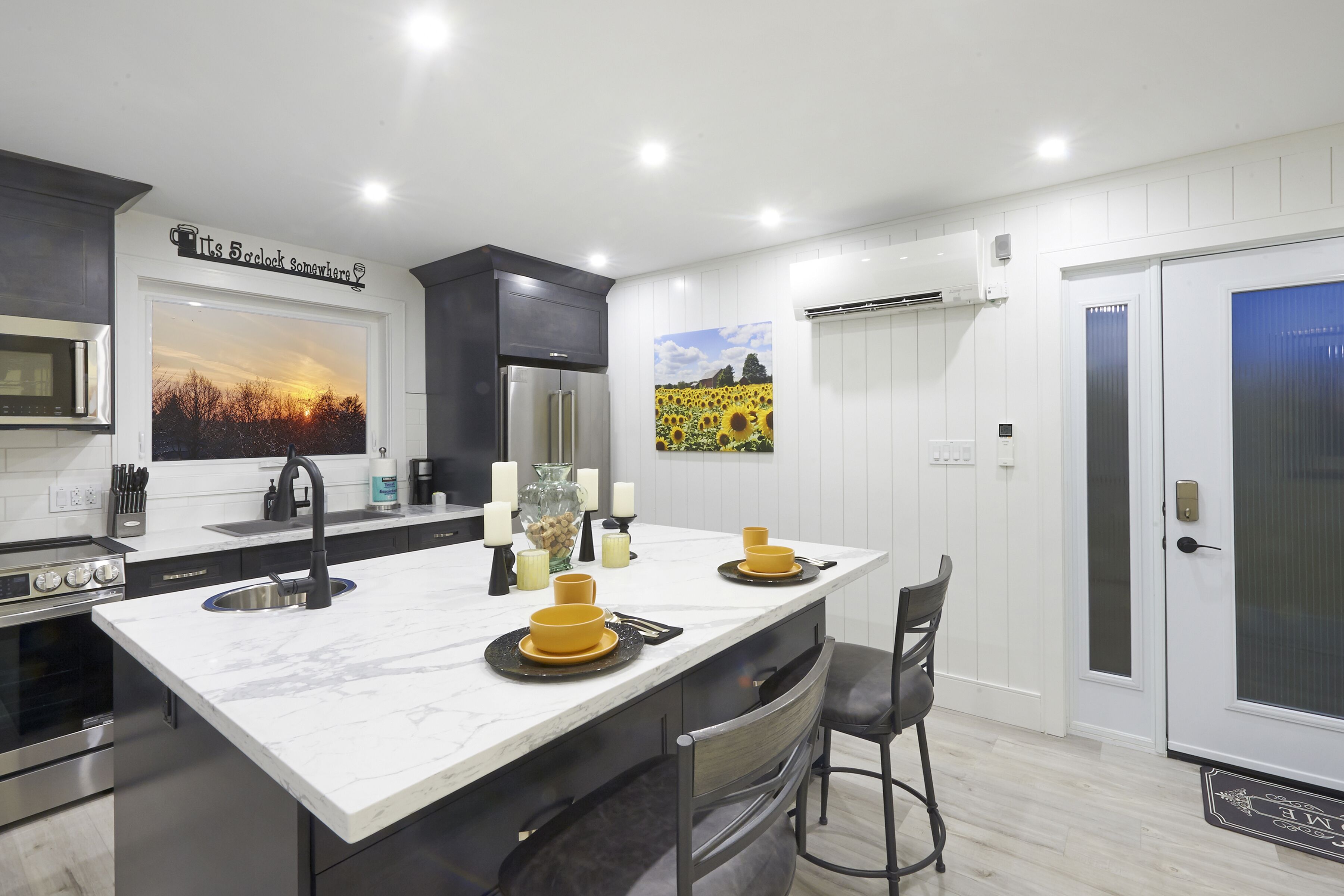 Una cocina moderna con una isla grande, electrodomésticos de acero inoxidable y vistas al atardecer a través de una ventana.