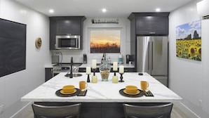 Une cuisine moderne dotée d’un îlot central, d’appareils électroménagers en acier inoxydable et offrant une vue sur le coucher de soleil par une fenêtre.
