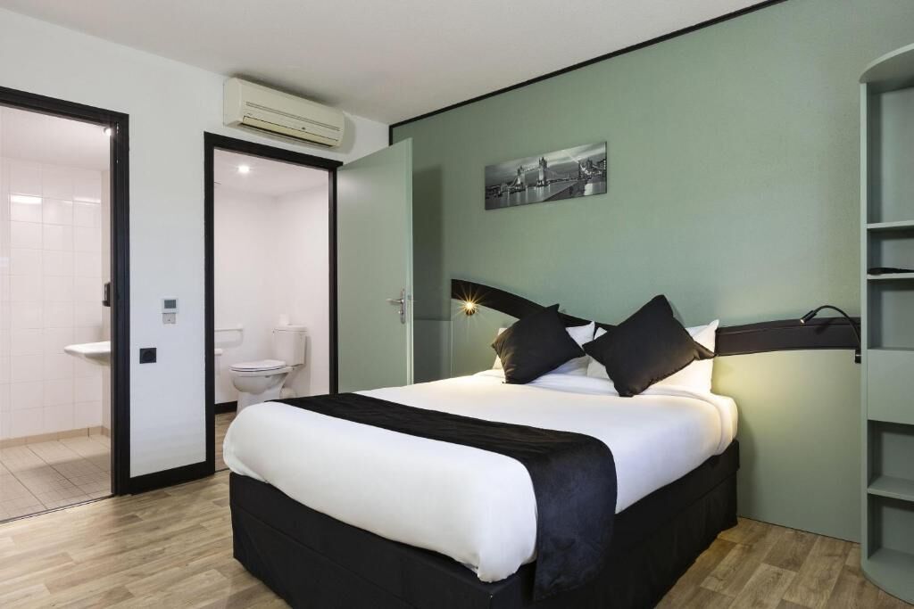 A bedroom with a bed, a bedside table, a wall-mounted picture, and a door leading to a bathroom.