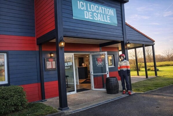 Um edifício com uma placa que diz 'ICI LOCATION DE SALLE' e uma pessoa em frente.
