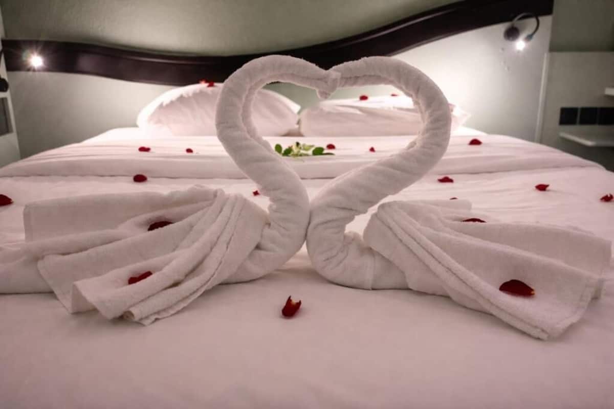 Una cama con ropa de cama blanca y una disposición de toallas con forma de corazón.
