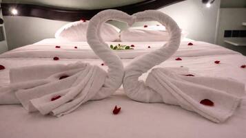 A bed with white linens and a heart-shaped towel arrangement.