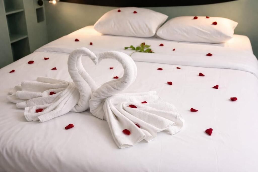 Una cama con una toalla dispuesta en forma de corazón y pétalos de rosa esparcidos.