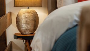 Een slaapkamer met een houten vloer, een ronde lamp op een houten voet en een bed met wit- en blauwe beddengoed, plus een hoofdeinde met meerdere kussens.