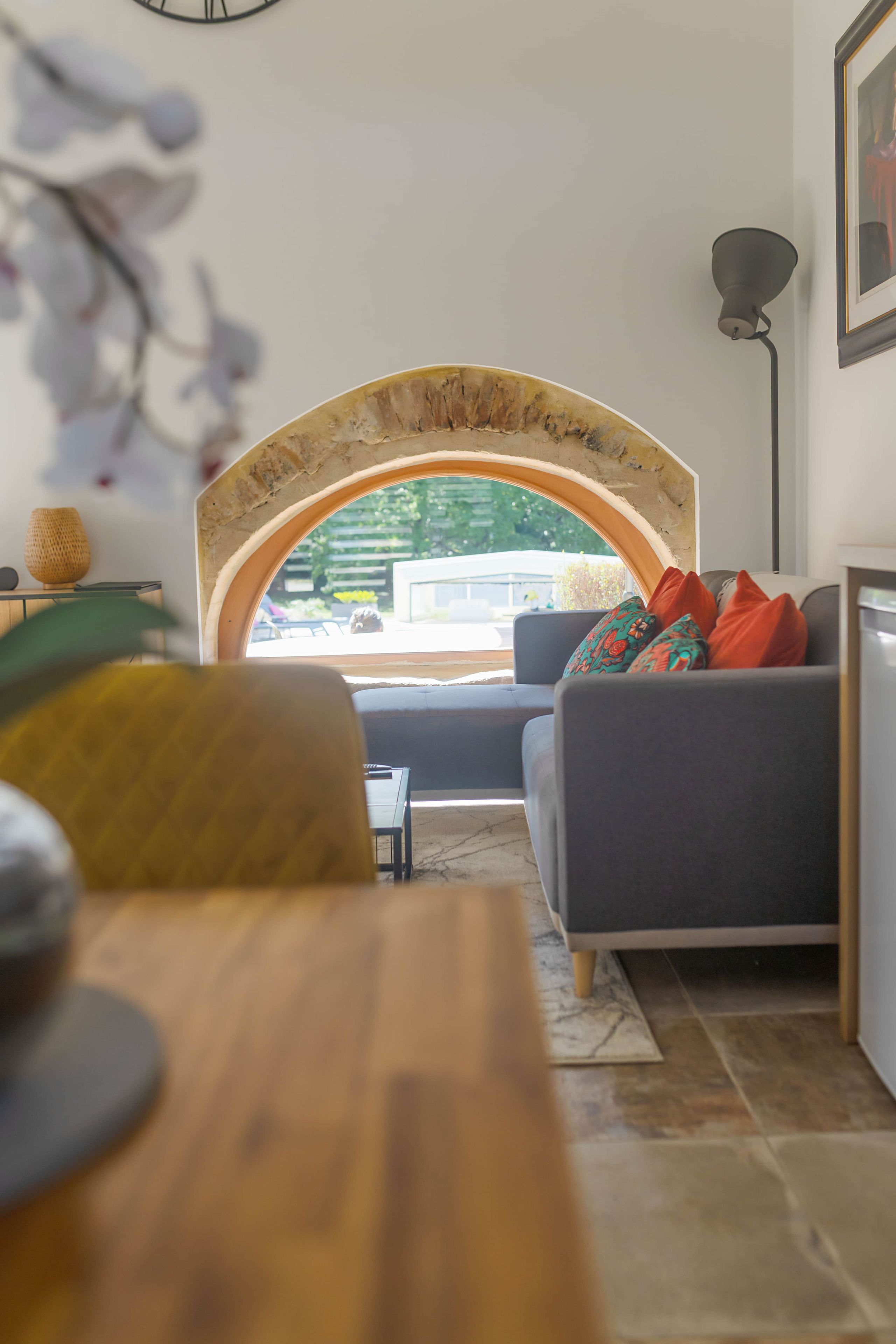Un salon avec un canapé, une table en bois et une vue à travers une fenêtre en arc de cercle.