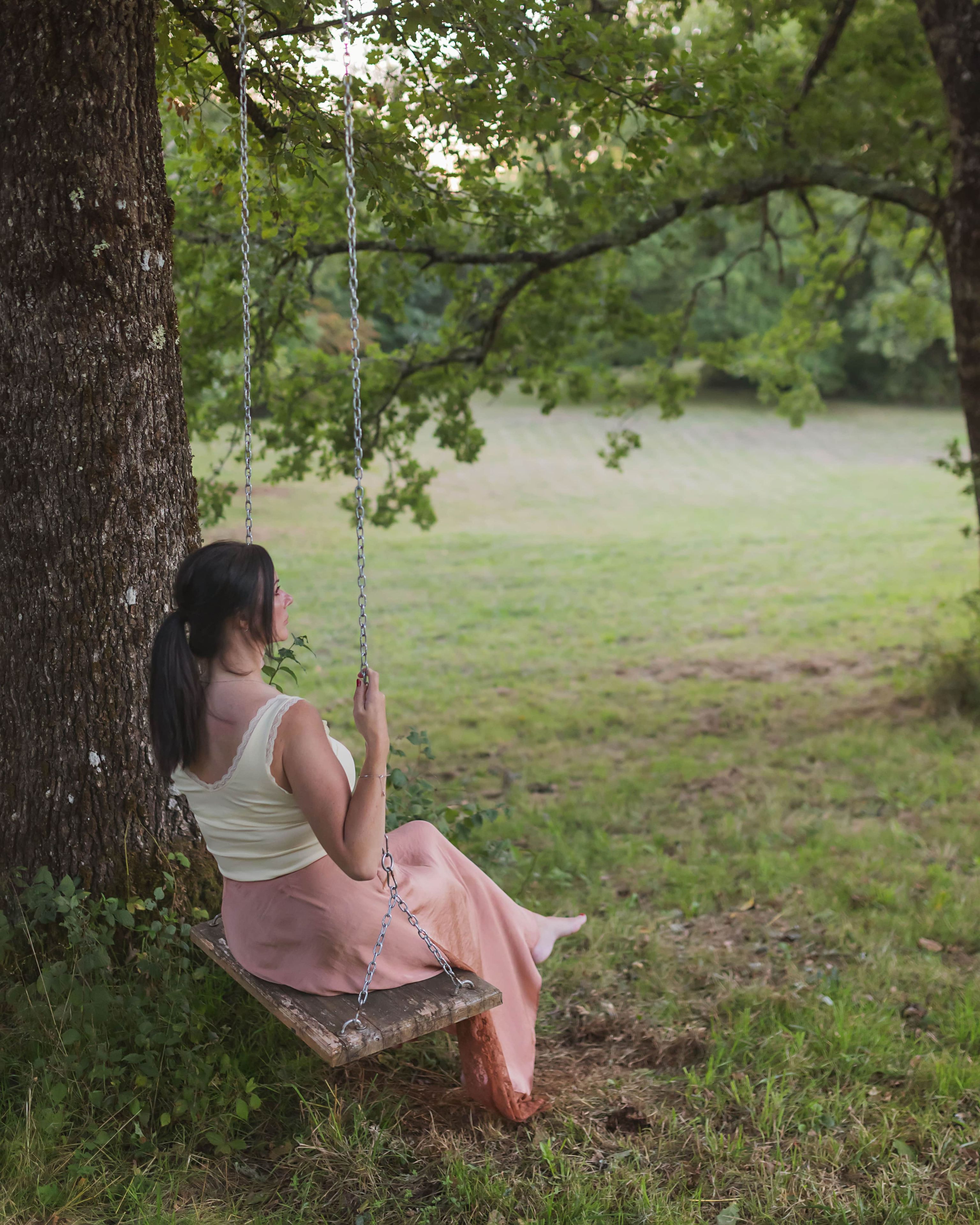 Eine Person sitzt auf einer Schaukel unter einem Baum in einer grünen Wiese.